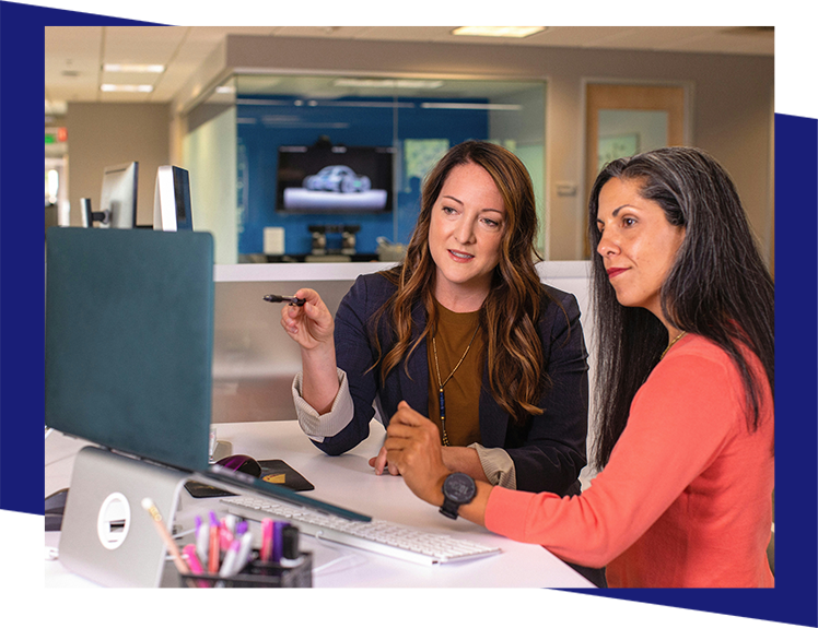 Two women sitting at a table looking at a computer screen.