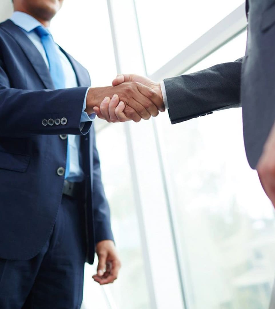 Two men in suits shaking hands over a window.